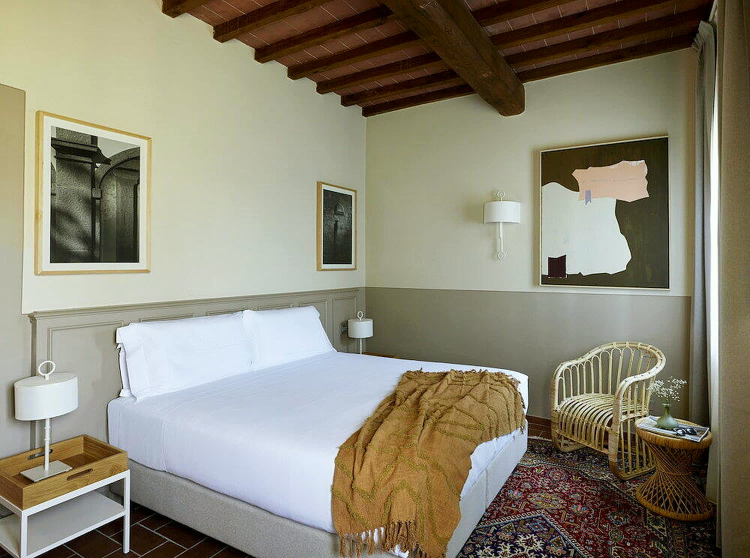 Camera con travi a vista e letto in lino bianco.