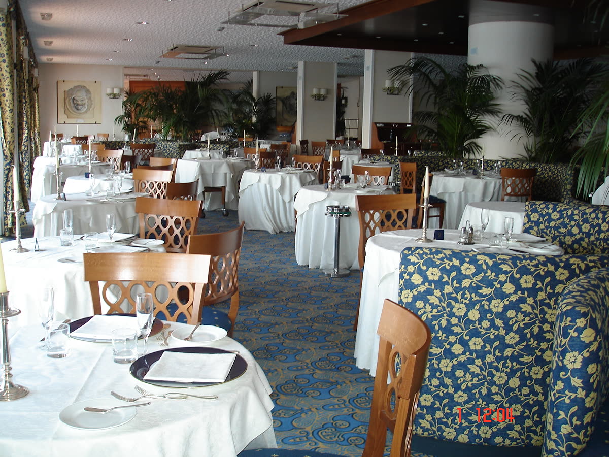 La sala ristorante apparecchiata, con moquette a disegno floreale.