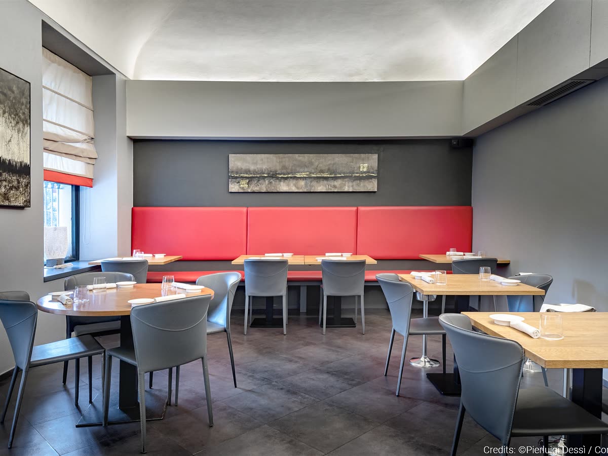 La sala del ristorante, con i tavoli apparecchiati e la parete grigia.