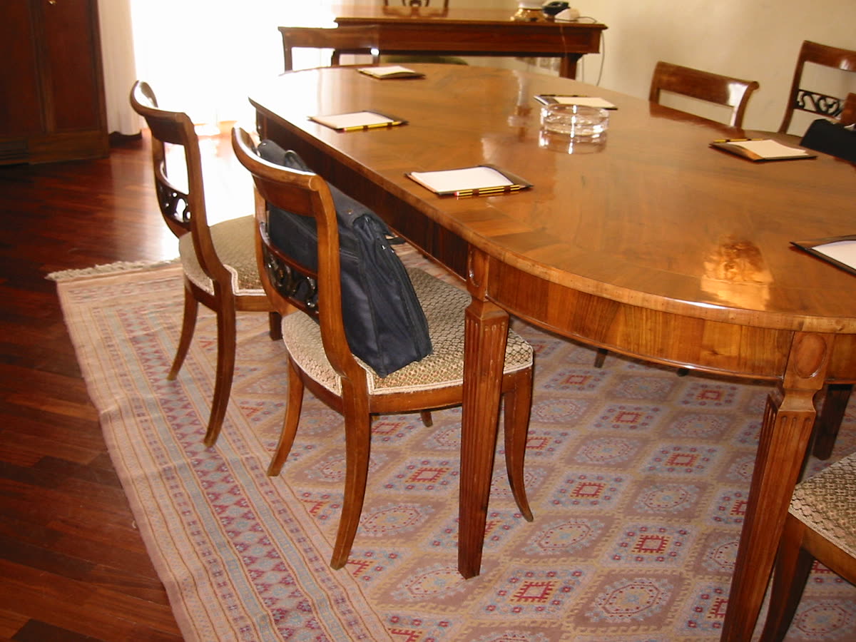 Sala riunioni con il tavolo ovale intarsiato e il tappeto.